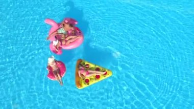 Aerial Top Down Fit kızları ve mayolu adam şişme pizza, çörek ve flamingo üzerinde yüzüyorlar. Arkadaşların tatilde pembe flamingo, çörek ve pizza yiyor.