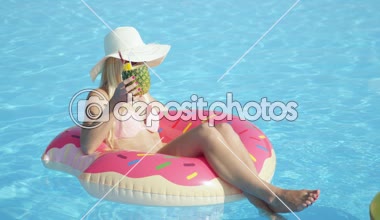 Ananas içki yudumlarken ve şişme pembe halka float rahatlatıcı ağır çekim yakın kadar mutlu sarışın kız. Yaz tatili havuzu pembe floatie üzerinde kokteyl içme zevk Bikini genç kadın