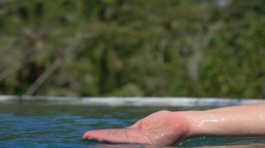 Ağır çekim yakın çekim: su ile oynarken, parmakları ile yakalamak ve orman resort sonsuzluk havuzunda içine dökülen beyaz el. İnsan palmiye su, scooping damla su yüzeyine düşen