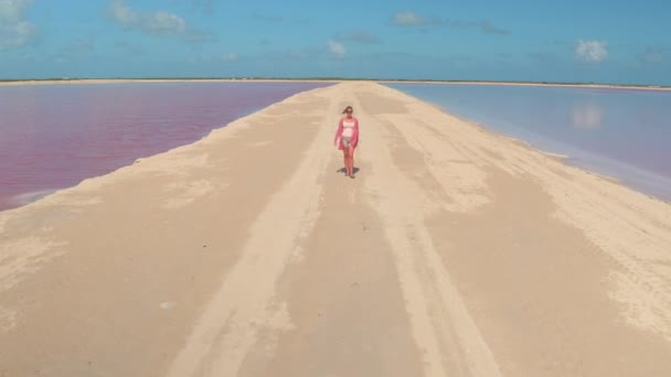クローズ アップ 魅力的な若い女性のホット晴れた日にメキシコでラス コロラド州の素晴らしいピンク湖を取り巻く砂の堤防に沿って歩きます サリナスに沿って散歩休暇観光女の子 — ストック動画