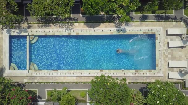 空中スローモーショントップダウン 暑い晴れた日にリフレッシュするために青いプールの水に頭を最初にジャンプ夏休みの女性 女の子でピンクビキニダイビングとスイミングで空のプールで高級リゾート — ストック動画