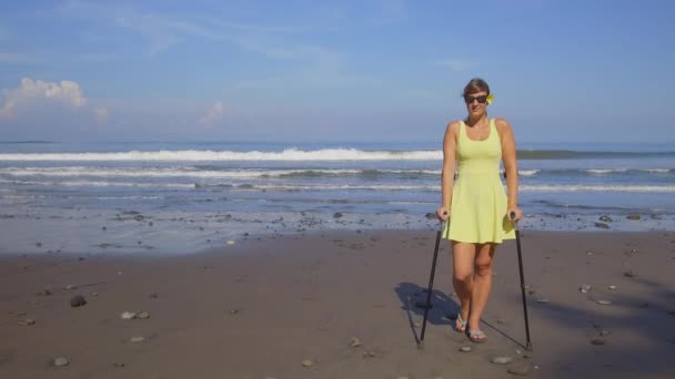 クローズ アップ 屈託のない強い自立した女性夏休みビーチに松葉杖で移動します グッド健康保険カバーを有する心配ないと休日を楽しむ砂浜の海岸に立っている女の子を笑顔 — ストック動画