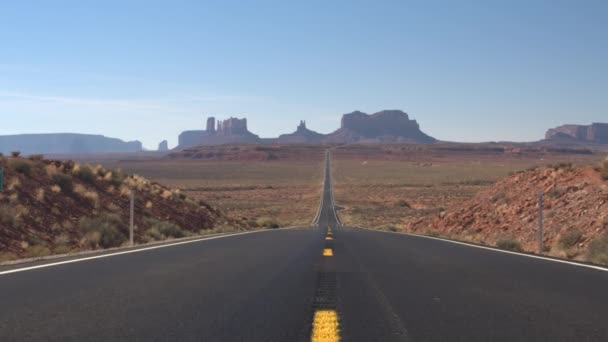 孤独的汽车沿着一条空荡荡的笔直道路驶向美国犹他州纪念碑谷的标志性山丘和梅萨山脉 旅行者前往令人惊叹的沙漠纪念碑山谷地标景观 — 图库视频影像