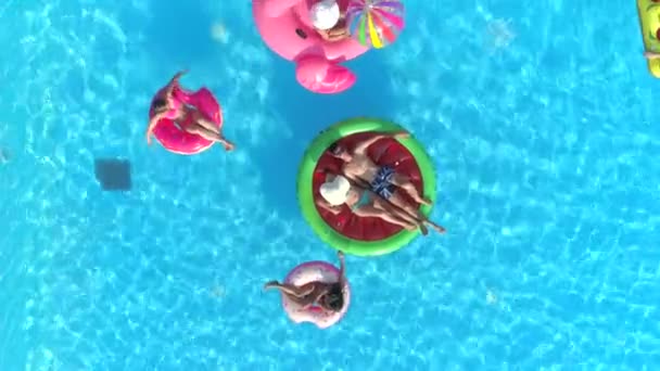 Von oben nach unten entspannen junge Mädchen und Jungen auf bunten Schwimmern, die auf dem Poolwasser schwimmen. glücklich lächelnde Freunde genießen den Sommerurlaub auf aufblasbaren Wassermelonen, Pizza, Flamingo und Donuts