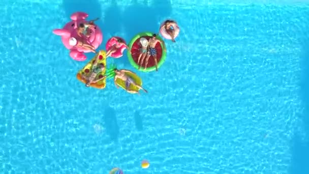 空中复制空间 好玩的女孩和男人躺在五颜六色的浮雕在游泳池 快乐的微笑的朋友享受暑假充气菠萝 比萨饼 火烈鸟 西瓜和甜甜圈漂浮 — 图库视频影像