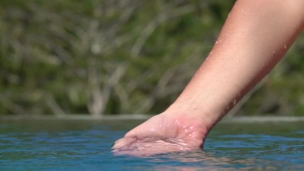 スローモーションをクローズ アップ 白人女性手水と遊ぶ 指でそれをキャッチ ジャングル リゾートのプールに注ぐ 水をすくいひと掌滴水の表面の上に落ちて — ストック動画