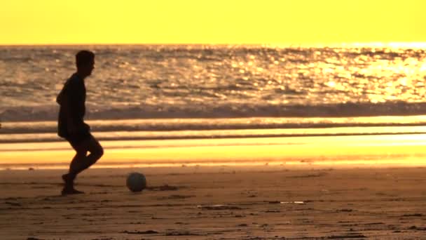 スローモーション クローズ アップ 陽気な地元の子供たちサッカー 濡れた砂浜に裸足を実行している 美しい黄金の光夕日でボールを蹴るします アジア子供夏のオレンジ色の日の出でゲームをプレイ — ストック動画