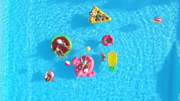 空中顶部 女孩和家伙玩在有趣的五颜六色的浮雕在游泳池玩球 愉快的朋友享受暑假在充气菠萝 比萨饼 火烈鸟 西瓜和甜甜圈漂浮 — 图库视频影像