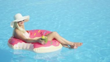 Ananas içki yudumlarken ve şişme pembe halka float rahatlatıcı ağır çekim yakın kadar mutlu sarışın kız. Yaz tatili havuzu pembe floatie üzerinde kokteyl içme zevk Bikini genç kadın