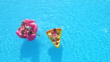 Aerial Top Down Fotokopi Uzayı: Mayo giymiş genç erkek ve kadınlar suda yüzen eğlenceli şişme pizza ve flamingo üzerinde uzanıyorlar. Mutlu arkadaşlar tatilde pembe flamingoyla eğleniyor ve pizza havuzda yüzüyor.