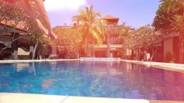 Slow Motion Close Up Lens: Yaz tatilindeki genç bir kadın sıcak güneşli bir günde serinlemek için önce mavi havuz suyuna atlıyor. Pembe bikinili kız lüks oteldeki boş havuza dalıyor.