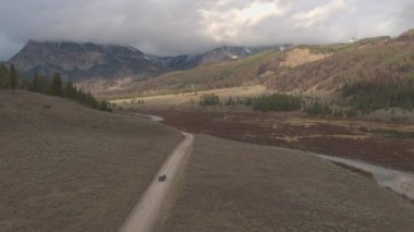 Anteni: çamurlu yol yalak üzerinde araba siyah Suv araba güzel Nehri Vadisi çam ağaçları görkemli kayalık Dağları Wyoming ABD doğru geçmiş. Off road jeep bulutlu Dağları altında çakıl yolda seyahat