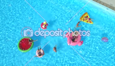Hava: neşeli arkadaşları su havuz partisinde renkli floaties fight. Oynak çocuklar ve kız alma selfies şişme pizza, halka, flamingo ve karpuz yüzen üzerinde ve su sıçramasına