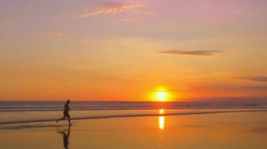 Ağır çekim, Close Up, Lens Flare: waterdrops dramatik Altın ışık günbatımında sıçramasına ıslak kum plaj boyunca çıplak ayakla çalışan bir genç adam. Adam doğal deniz kıyısı güneşli yaz akşamı koşu