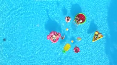 Hava aşağı üst: kızlar ve çocuklar ile top oynarken eğlenceli renkli floaties Havuzu. Neşeli arkadaşları yaz tatile şişme ananas, pizza, flamingo, karpuz ve halka yüzen zevk