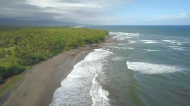 Yemyeşil palmiye ağacı orman ile büyümüş muhteşem Bali kıyı şeridi üzerinde uçan hava. Rüya gibi kumsalda fırtınalı bir gün önce yağmur insanlar. Çalkantılı beyaz köpüklü okyanus dalgalarının sıçramasına karşı Rocky resif