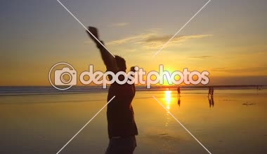 Ağır çekim, Close Up, siluet: genç adam güzel kumsalda büyülü Altın ışık günbatımında kaldırdı kollarını iplik heyecanlı. Mutlu adam heyecanla tezahürat. Yaz tatillerini insanlar