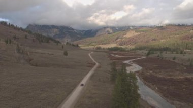 Anteni: çamurlu yol yalak üzerinde araba siyah Suv araba güzel Nehri Vadisi çam ağaçları görkemli kayalık Dağları Wyoming ABD doğru geçmiş. Off road jeep bulutlu Dağları altında çakıl yolda seyahat