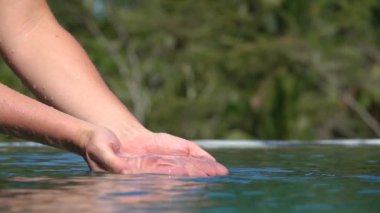 Ağır çekim, Close Up, Dof: düz havuz suyu onun eline scooping ve sıçramasına, parlak su yüzeyi isabet waterdrops düşüyor kadın. Lüks resort tropikal adada oynayan genç kız