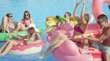 Ağır çekim yakın kadar mutlu gülümseyen öğrenciler bahar havuz partisinde renkli floaties fight su tabancası var. Şişme flamingo pizza karpuz ve halka eğlenceli neşeli genç insanların yok