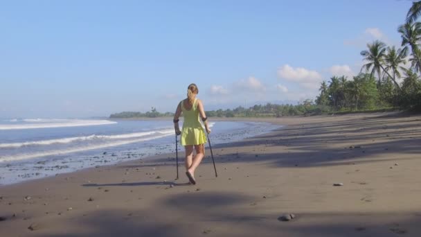 强大的独立妇女走在沙滩上的沙滩上暑假在热带岛屿巴厘岛 女孩腿受伤漫步在岸边与棕榈树享受假期 — 图库视频影像