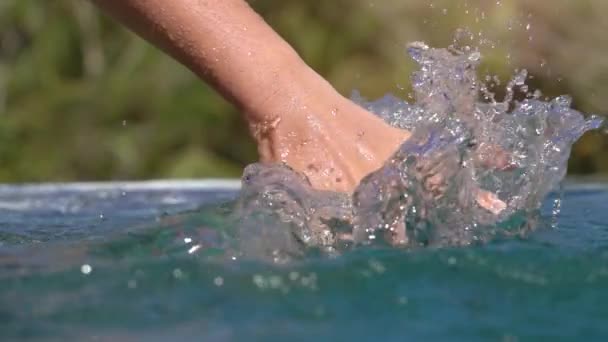 スローモーション閉じるを認識できない若い女性をドラッグ 水を通して 彼女の手をスライド屋外インフィニティ プールで飛散水滴を表面します 熱帯の島でリラックスした夏の休暇の女の子 — ストック動画