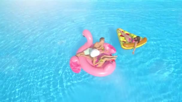 空中情人闪光 穿着泳衣的年轻女孩和小伙子躺在有趣的充气披萨和漂浮在水面上的粉色火烈鸟上 假期快乐的朋友们在游泳池里享用粉色火烈鸟和比萨饼 — 图库视频影像