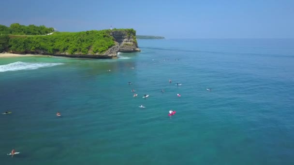 Anténa: Surfaři, plovoucí na vodě, čeká na vlny v řadě pod vysoký skalní útes. Luxusní turistické středisko s golfové hřiště, bungalovy, kabina domy a hotely ve svěží zelené džungle v Bali