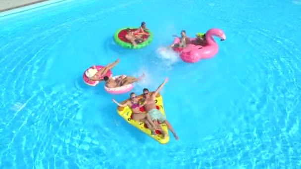 Antenne: Fröhliche Freunde amüsieren sich auf bunten Festwagen beim sommerlichen Poolfest. verspielte Jungs und Mädchen, die Wasser planschen und Selfies auf aufblasbaren Pizza-, Donut-, Flamingo- und Wassermelonenwagen machen