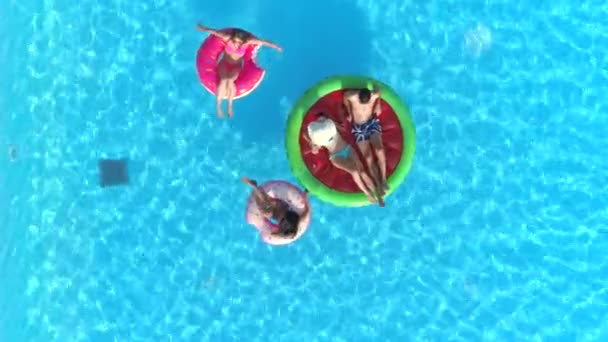 Letecký shora dolů mladé dívky a chlap pokládání a relaxaci na barevné floaties plovoucí na povrchu vody bazénu. Happy usměvaví přátelé těší letní dovolenou na nafukovací plováky meloun a prstencového grafu