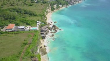 Hava: lüks turizm tesisi çarpıcı Bali adasında yüksek kayalık okyanus uçurumun kenarına, yukarıda uçan. İnsanlar güzel güneşli yaz gününde zümrüt deniz manzaralı otel sonsuzluk havuzu yüzme