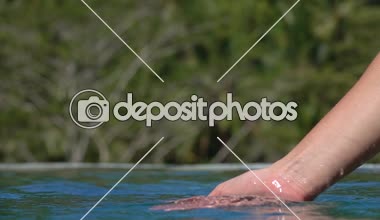 Ağır çekim yakın çekim: su ile oynarken, parmakları ile yakalamak ve lüks resort sonsuzluk havuzunda içine dökülen beyaz el. İnsan palmiye su, scooping damla su yüzeyine düşen