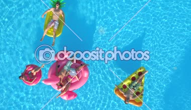 Hava üst aşağı rahat kızlar ve çocuklar üzerinde renkli floaties havuzu su üzerinde yüzer döşeme. Yaz tatili şişme ananas, pizza, flamingo ve halka yüzen zevk mutlu gülümseyen arkadaşlar