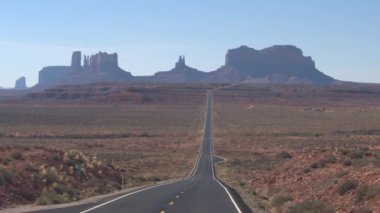 İlk kişi görünümü ikonik Monument Valley landmark Utah ABD doğru düz boş bir yol boyunca sürüş. Monument Valley çöl yatay olarak sarı lekeler ile yeni otoyol yolda seyahat Pov