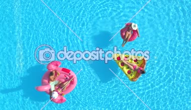 Aerial Top Down Fit kızları ve mayolu adam şişme pizza, çörek ve flamingo üzerinde yüzüyorlar. Arkadaşların tatilde pembe flamingo, çörek ve pizza yiyor.