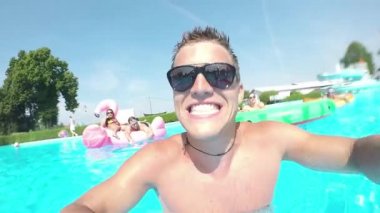 Selfie video havuzunda renkli floaties üzerinde arkadaşlarınızla yapan Slow Motion Selfie komik genç adam. Gülümseyen ve şişme pizza flamingo ve karpuz yüzen yaz tatili zevk mutlu gençler