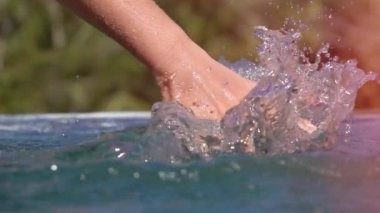 Ağır çekim yakın Lens Flare Up: Ayrıntı sürükleyerek ve su yüzeyi kayar ve sonsuzluk havuzunda waterdrops sıçramasına genç kadın el. Tropik adada rahatlatıcı yaz tatillerini üzerinde kız