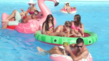 Ağır çekim yakın kadar mutlu gülümseyen öğrenciler bahar havuz partisinde renkli floaties fight su tabancası var. Neşeli gençler eğleniyor şişme flamingo, karpuz ve halka