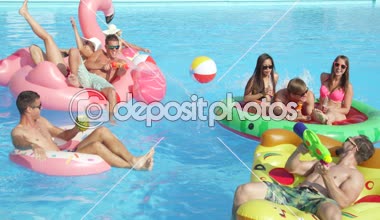 Ağır çekim yakın kadar mutlu gülümseyen öğrenciler bahar havuz partisinde renkli floaties fight su tabancası var. Şişme flamingo pizza karpuz ve halka eğlenceli neşeli genç insanların yok