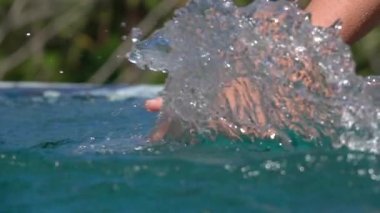 Ağır çekim kadar yakın: Tanınmayan genç kadın sürükleyerek ve eline su yüzeyinden kayar ve sonsuzluk havuzunda waterdrops sıçramasına. Tropik adada rahatlatıcı yaz tatillerini üzerinde kız