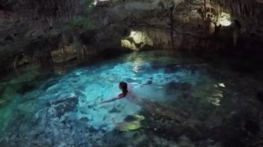 Soluk kesici yeraltı mağarasında turkuaz havuzda yüzen genç bir kadın. Aktun Chen 'in Meksika' daki obruk çukurunda sarkıtların ve dikitlerin büyüleyici mimarisini keşfeden turistler