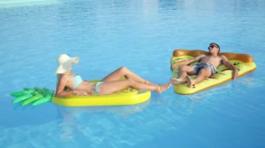 Yakın: döşeme ve pizza ve ananas floaties havuzunda rahatlatıcı genç çift uygun. Kız ve erkek arkadaşı yaz tatile eğlenceli renkli su içerisinde yüzen yüzen zevk sıcak güneşli bir gün
