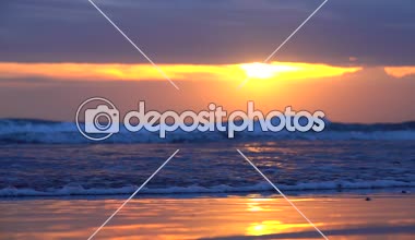 Ağır çekim, Close Up: kumlu plaj yansıtan dramatik gökyüzü sunset Bulvarında tropikal ada önce Bali ıslak. Güzel turuncu alacakaranlıkta sıçramasına mavi okyanus dalgaları. Dalgalanan deniz sahil güneş doğarken yıkama