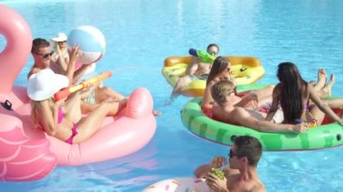 Ağır çekim yakın çekim: sıcak yaz aylarında havuz partisinde renkli floaties üzerinde zevk oynak gülümseyen arkadaşlar. Gençler neşeli şişme pizzaya eğleniyor, flamingo, karpuz ve halka yüzen