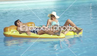 Yakın: döşeme ve pizza ve ananas floaties havuzunda rahatlatıcı genç çift uygun. Kız ve erkek arkadaşı yaz tatile eğlenceli renkli su içerisinde yüzen yüzen zevk sıcak güneşli bir gün
