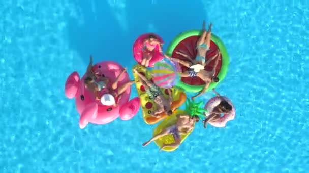 von oben nach unten lustige Mädchen und Jungs, die mit Ball auf bunten Schwimmern im Pool spielen. Lächelnde Freunde genießen den Sommerurlaub auf aufblasbaren Ananas, Pizza, Flamingo, Wassermelone, Donut schwimmt
