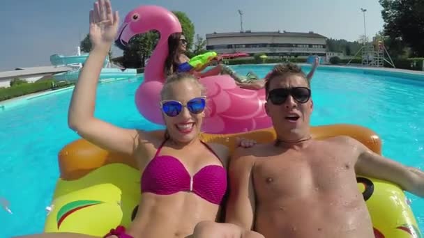 スローモーション レンズ フレア Selfie 笑顔のカップルと友人はプールでカラフルな Floaties を楽しんでします 夏水膨脹可能なピザの上の戦いを持つこと幸せな 代の若者 フラミンゴ — ストック動画