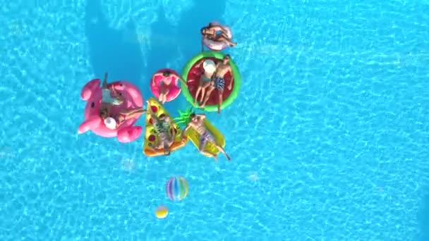 コピー空間 遊び心のある女の子とプールでカラフルな Floaties を置く男 インフレータブルのパイナップル フラミンゴ スイカ ドーナツの山車に夏休みを楽しんでいる笑顔の幸せの友人 — ストック動画