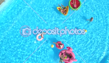 Hava: neşeli arkadaşları su silah olan havuz partisinde renkli floaties fight. Oynak çocuklar ve su ve hava ile şişirilen pizza, halka, flamingo ve karpuz yüzen üzerinde eğlenmek kızlar