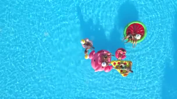 空中顶部 快乐的女孩和男人在游泳池里玩球 愉快的微笑的朋友享受暑假在充气菠萝 比萨饼 火烈鸟 西瓜和甜甜圈漂浮 — 图库视频影像